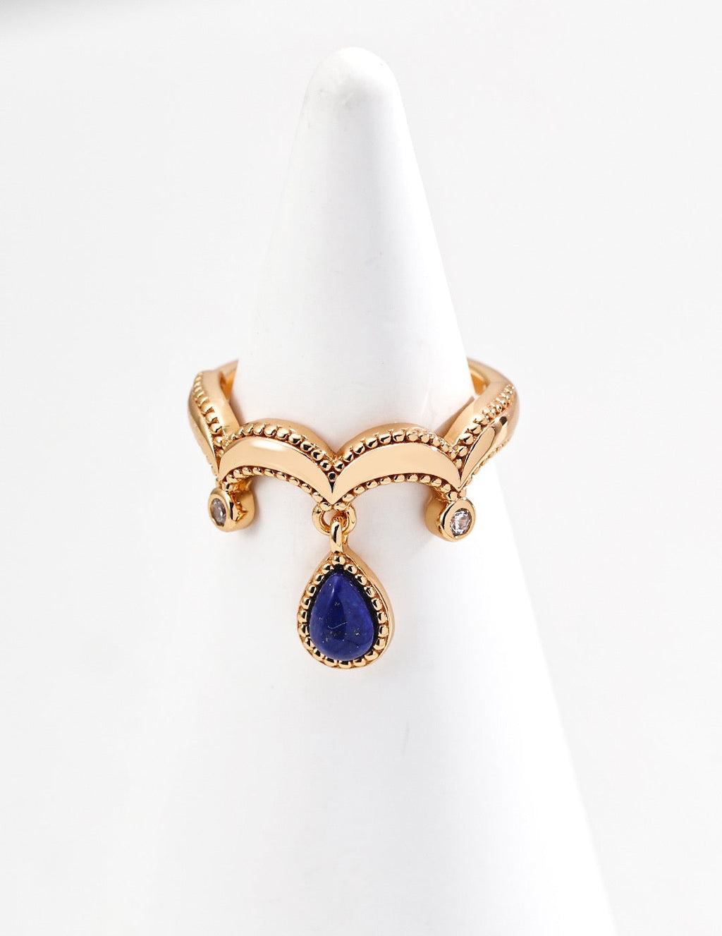 Gold crown charm ring with lapis lazuli teardrop pendant and crystal accents on a white ring display